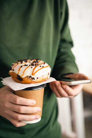 A cup of coffee, a donut and a smartphone in male hands, close-up.の写真素材