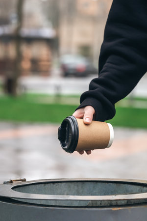 A man throws a paper disposable cup into the trash can in the park.の写真素材