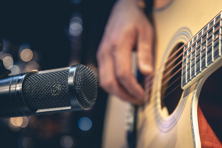 Male musician playing acoustic guitar behind microphone in recording studio.の写真素材