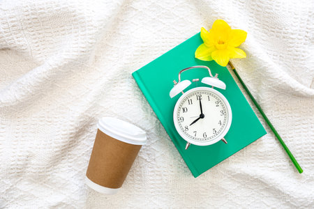 Book, alarm clock, coffee cup and flower in white bed, top view.の写真素材