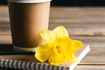 Paper disposable cup, notebook and yellow flower on a wooden blurred background.の写真素材