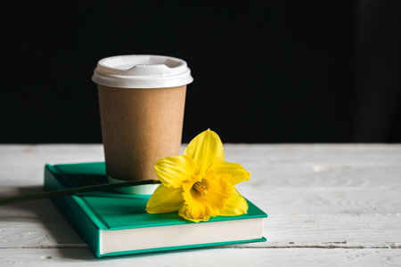 Paper cup, book and yellow flower on a blurred wooden background.の写真素材