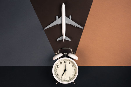 White alarm clock and airplane model on a paper background, top view.