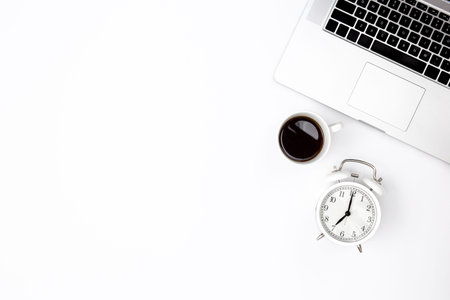 White background with laptop, alarm clock and black coffee cup, top view.