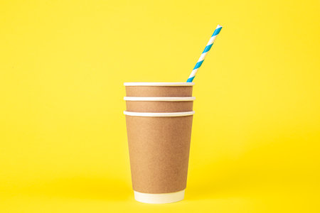 Three paper disposable cups and a striped paper straw on a yellow background.の写真素材