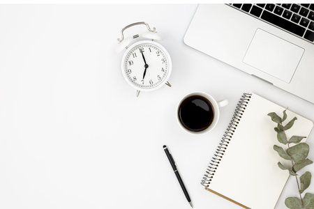 White background with laptop, notepad, alarm clock and black coffee, top view.