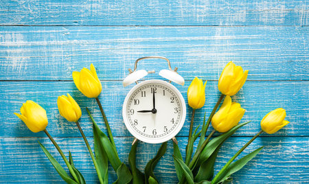 White alarm clock and yellow tulips on a blue background, top view.