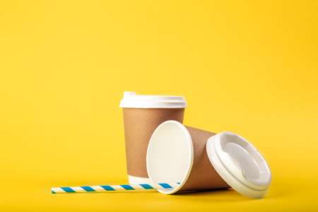 Disposable cups and a striped straw on a yellow background isolated.の写真素材