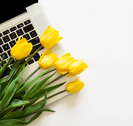 Bouquet of yellow tulips and a laptop on a white background isolated, top view.の写真素材