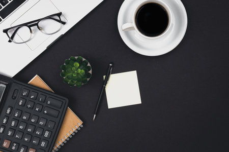 Laptop, glasses, coffee cup and calculator on a black background, top view.の写真素材