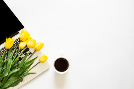 Laptop, a cup of coffee and a bouquet of tulips on a white background, top view.の写真素材