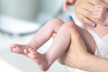 Newborn baby in mothers hands, legs close-up.