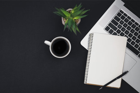 Laptop, coffee cup and notepad on black background, top view.