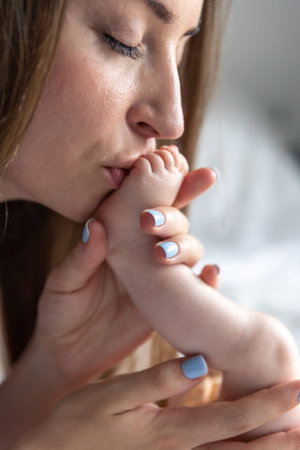 Caring young mother kissing babys feet, close up.