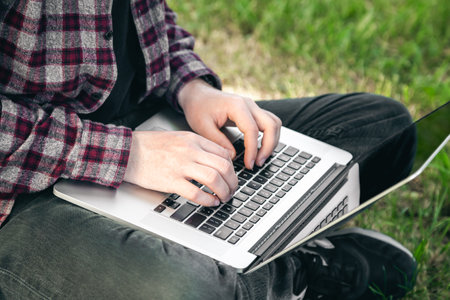 Man in the park sitting on the grass with a laptop, close-up hands and laptop.の写真素材