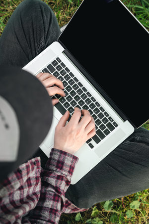 A man using laptop with blank screen while sitting on green grass, top view.