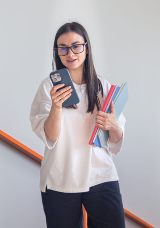Young woman in glasses with smartphone and notepads.