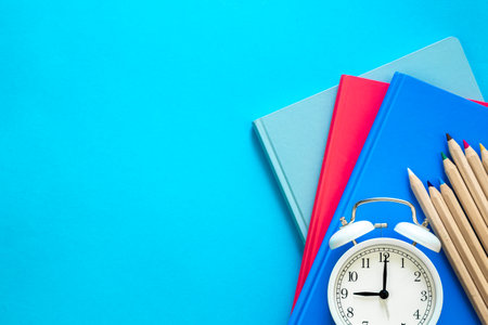 Notebooks, pencils and an alarm clock on a blue background, top view.の写真素材
