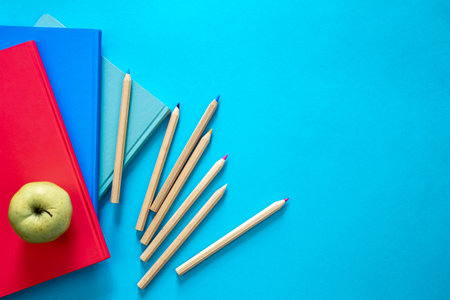 Notebooks, apple and pencils on a blue background, top view.の写真素材