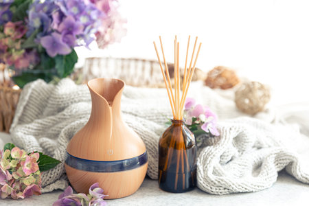 Aroma oil diffuser lamp, flowers and knitted element on a blurred background.