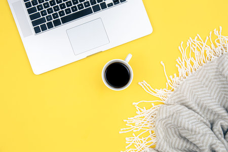 Laptop, a cup of coffee and a plaid on a yellow background.