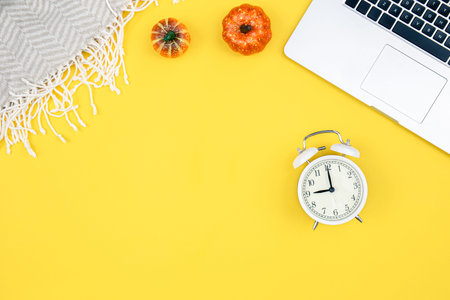 Autumn yellow flat lay with a laptop, pumpkins and alarm clock.