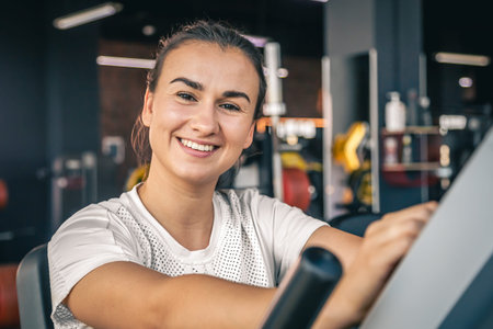 A tired young brunette woman in sportswear in the gym is engaged on a bike.
