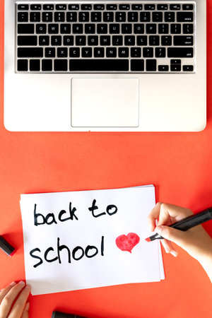 Back to school the childs hand writes in a paper on a red background.