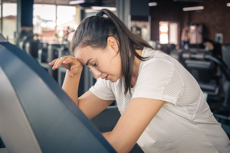 Tired young woman on treadmill at gym.