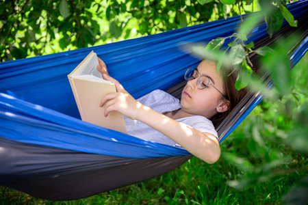 Cute girl reading a book in a hammock in the garden.の写真素材