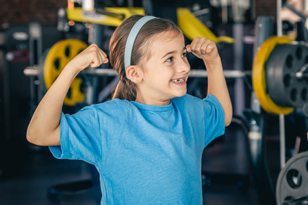 Charming little girl is shows her biceps, working out at gym.の写真素材