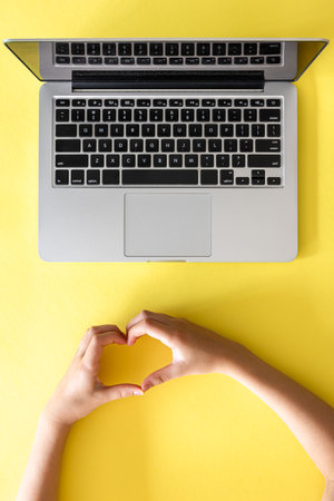 Laptop on yellow background and heart symbol shape with kid hands.の写真素材