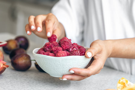 A bowl with raspberries in female hands on a white kitchen table.の写真素材