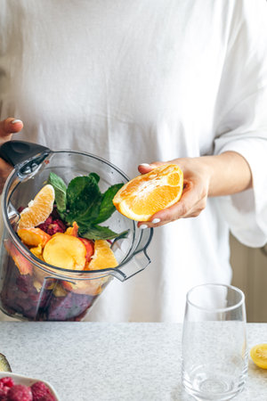 A woman squeezes orange juice into a blender, making a fruit smoothie.の写真素材
