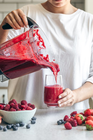 A woman pours a berry smoothie from a blender into a glass.の写真素材