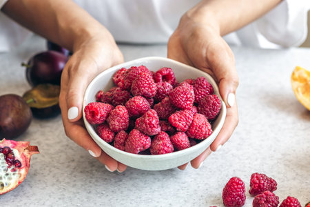 A bowl with raspberries in female hands on a white kitchen table.の写真素材