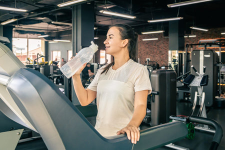 A young woman on a treadmill at the gym with a bottle of water.