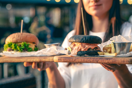 A young woman holding fast food burgers on a wooden trays outdoor.の写真素材