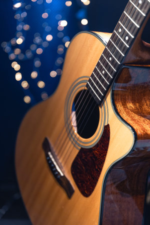Close-up, acoustic guitar on a dark background with bokeh lights.