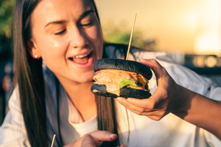 A young woman eating burger in street cafe, close up.の写真素材