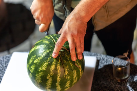 A man cuts a watermelon on a blurred kitchen background.の写真素材