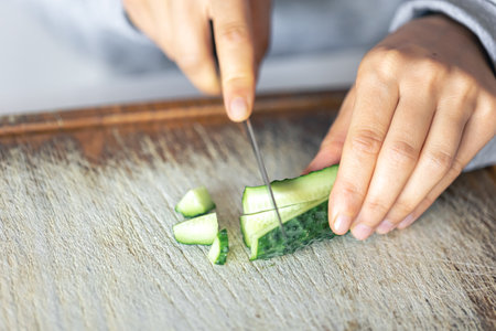 A woman cuts a fresh cucumber on a cutting board.の写真素材