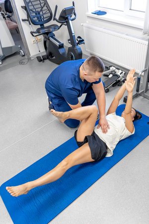 Woman doing gymnastics with help of his young physical therapist.