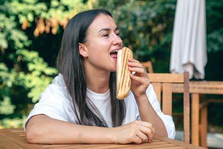 A young woman eats a hot dog on a cafe terrace.