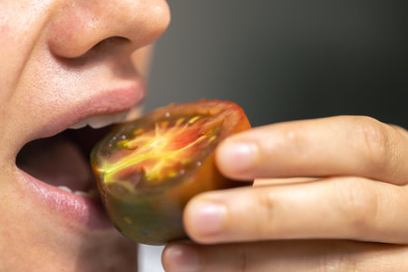 Detailed shot of a woman bites ripe tomato.の写真素材