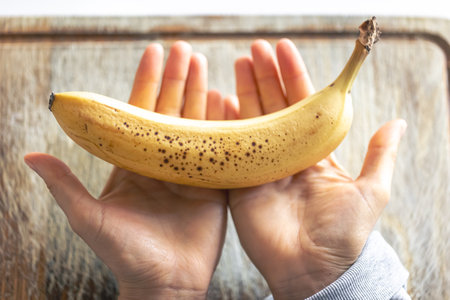 Ripe banana in female hands in the kitchen close-up.の写真素材