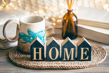 Cozy composition with wooden word Home and cup on blurred background.