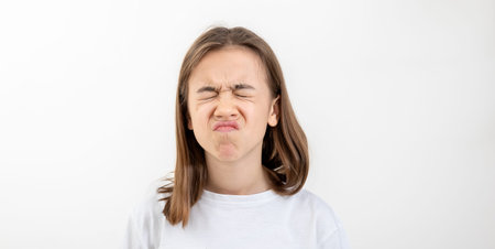 A teenager girl grimaces with displeasure on a white background, isolated.