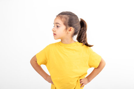 Serious little girl holding hands on her waist on a white background isolated.の写真素材