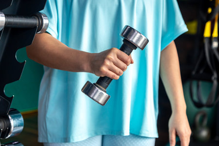 Small dumbbell in the hands of a woman in the gym, close up.